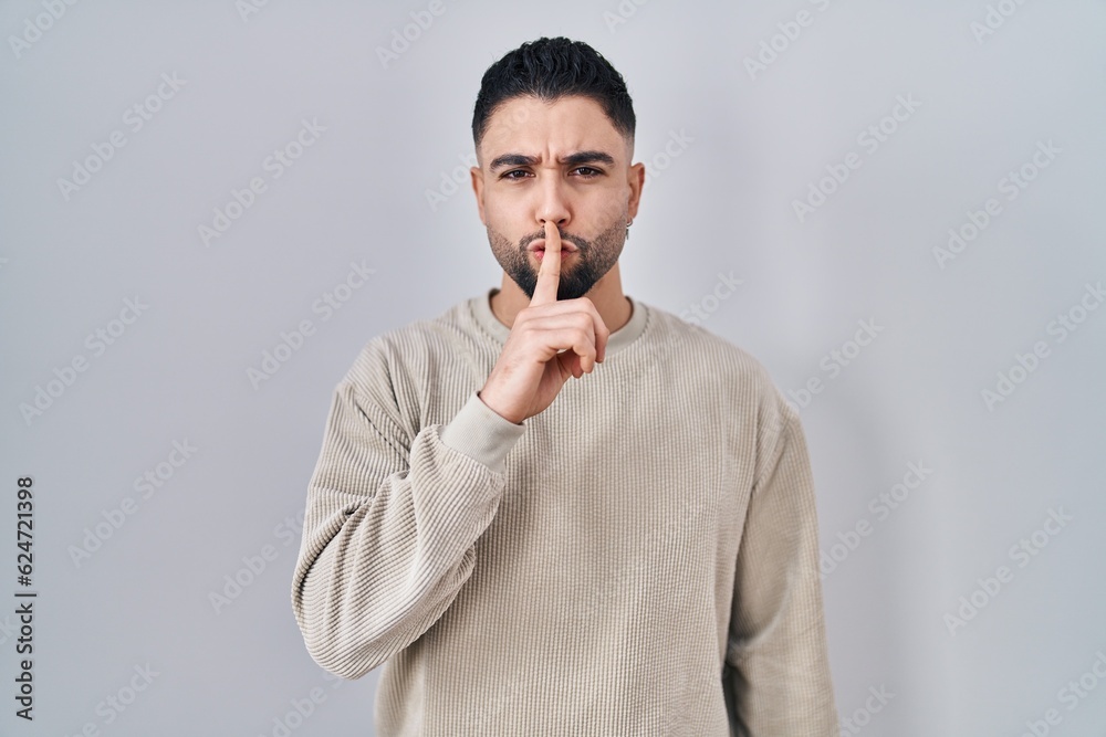 Wall mural young handsome man standing over isolated background asking to be quiet with finger on lips. silence