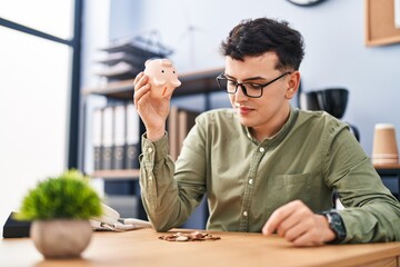 Young non binary man business worker emptying piggy bank at office