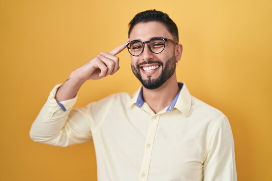 Hispanic young man wearing business clothes and glasses smiling pointing to head with one finger, great idea or thought, good memory