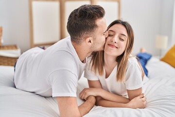 Man and woman couple lying on bed hugging each other and kissing at bedroom