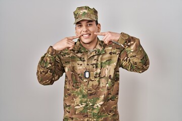 Young arab man wearing camouflage army uniform smiling cheerful showing and pointing with fingers teeth and mouth. dental health concept.