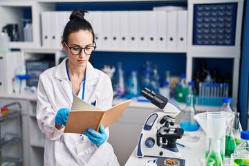 Young caucasian woman scientist reading book at laboratory