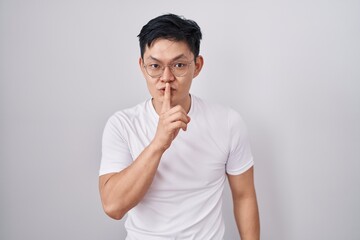 Fototapeta na wymiar Young asian man standing over white background asking to be quiet with finger on lips. silence and secret concept.