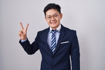 Young asian man wearing business suit and tie showing and pointing up with fingers number two while smiling confident and happy.