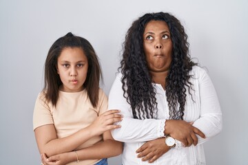 Mother and young daughter standing over white background making fish face with lips, crazy and...