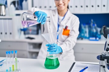 Fototapeta premium Young hispanic woman scientist measuring liquid at laboratory