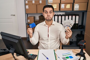 Young hispanic man with beard working at small business ecommerce holding banknotes and credit card...