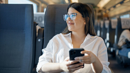 Young beautiful hispanic woman smiling using smartphone sitting inside train wagon