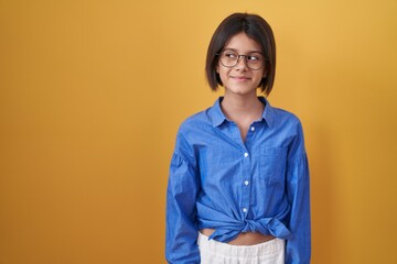 Young girl standing over yellow background smiling looking to the side and staring away thinking.