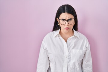 Young brunette woman standing over pink background skeptic and nervous, frowning upset because of problem. negative person.