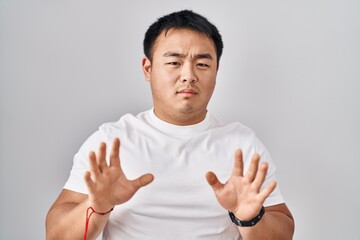 Young chinese man standing over white background moving away hands palms showing refusal and denial with afraid and disgusting expression. stop and forbidden.