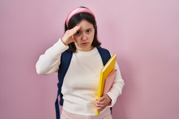 Woman with down syndrome wearing student backpack and holding books worried and stressed about a problem with hand on forehead, nervous and anxious for crisis