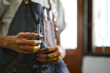 Art, education, creativity and people concept. Male artist hands soiled with watercolor paints holding brushes