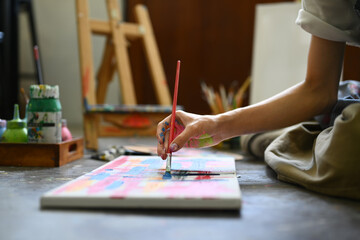 Male artist sitting on floor in art studio and painting on canvas with watercolors. Creative hobby...