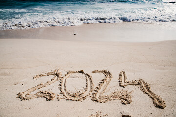 2024 written in white sand on tropical beach, happy New Year