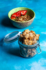 Healthy breakfast with granola and fresh strawberries served in a bowl on a blue background. Minimalistic composition with plate, spoon and natural morning light.