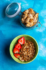 Healthy breakfast with granola and fresh strawberries served in a bowl on a blue background. Minimalistic composition with plate, spoon and natural morning light.