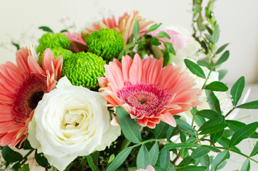 festive bouquet of white roses, pink gerberas and carnations in a frame of green twigs on a light background. Birthday. Mother's Day. The concept of holiday flowers. Selective focus.