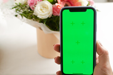 A phone with a green screen next to a festive bouquet of white roses, pink gerberas and carnations....
