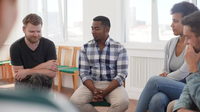 Panning shot of group therapy session with diverse people sharing sad problems and stories. Multicultural men and women sitting in circle talking about mental health issues and looking for support.