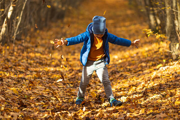 Happy little boy has fun in beautiful autumn park on warm sunny fall day. Child plays with golden maple leaves. Autumn foliage. Sun rays through the trees