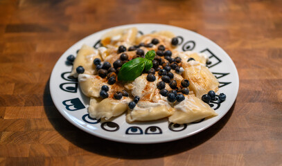 Traditional polish sweet cheese pierogi with blueberries, whipped cream, cinnamon and some basil decoration. Plate with sweet handmade dumpling dessert lunch or dinner on wooden table.