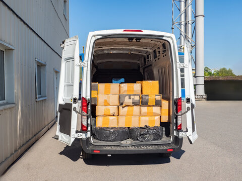 Minivan logistics company. Cargo vehicle with boxes. Minivan near logistics center. Large parcels in back of car. Minivan for provision of logistics services. White cargo vehicle near hangar