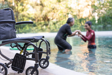 Selective focus off wheelchair background of physical therapist helping senior woman in aqua, old...