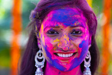 Head shot of young indian girl with holi color applied on face during holi festival celebration -...