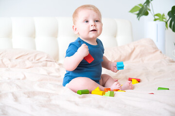 baby boy in blue bodysuit playing with colorful wooden eco toys on bed
