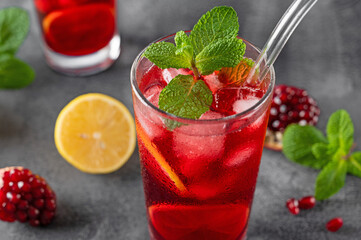 Iced red lemonade drink with fresh mint, sugar syrup and pomegranate juice in glass on a dark concrete background. Refreshing summer drink. Copy space.