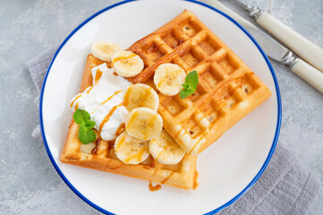 Waffles with banana, whipped cream and salty caramel on a gray concrete background.