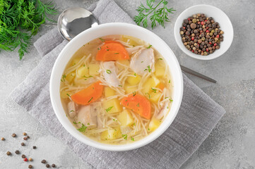 Chicken soup with noodles and vegetables in white bowl on a gray concrete background.