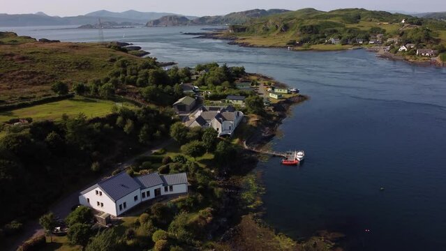 A beautiful drone shot following a Scottish island shoreline panning up to reveal boats, holiday properties and the rest of the Island&rsquo;s waterways, including a ferry crossing. Shot on ilse of Luing