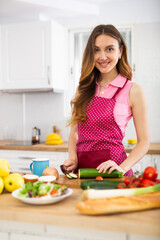 Cheerful young woman preparing vegetable salad for dinner at home