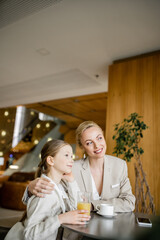 happy mother and daughter spending quality time, blonde woman hugging preteen girl and looking away near beverages and smartphone, working parent and kid, modern parenting, family bonding