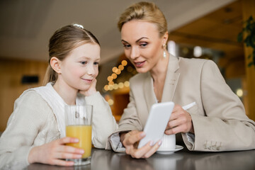 mother and daughter spending time together, blonde woman holding smartphone near daughter, working parent and child, modern parenting, family bonding, balanced lifestyle
