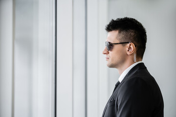 professional headshots, bodyguard service, side view of handsome man in sunglasses and black suit with tie, hotel safety, security management, surveillance and vigilance, uniformed guard on duty