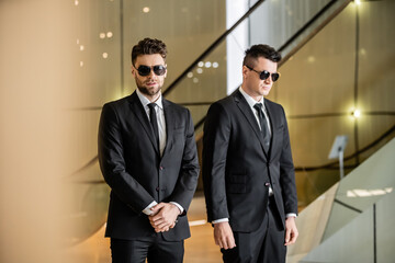 security management of luxury hotel, two handsome men in formal wear and sunglasses, bodyguards on duty, safety measures, vigilance, suits and ties, private security, strong guards