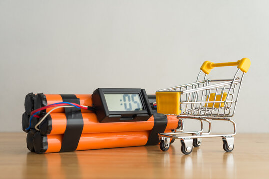 Shopping trolley on time bomb white wall background. Economic recession crisis, inflation rise, core retail sales decrease, goods price up, consumer confidence and consumer price index CPI decrease.