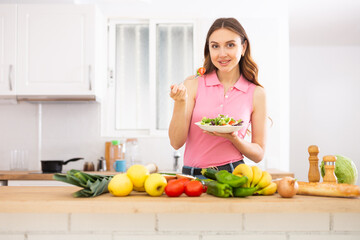 Obraz na płótnie Canvas Cheerful woman eating vegetable salad at home