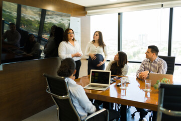 Pregnant woman standing by businesswoman addressing to team in meeting room