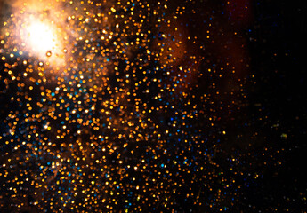 Defocused abstract background with shiny golden sparkles with bright backlight