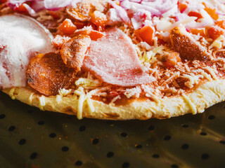 Uncooked meat pizza on a metal tray ready for cooking. Ready made Italian style meal.