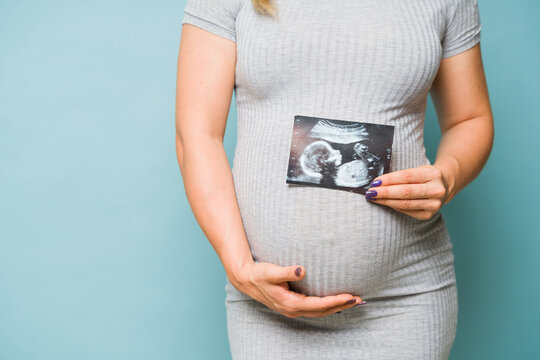 Close up of a pregnant woman holding a picture of her ultrasound next to her belly in a studio