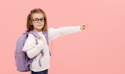 Portrait of a schoolgirl with textbooks and a backpack on a pink background pointing to the right. Back to school