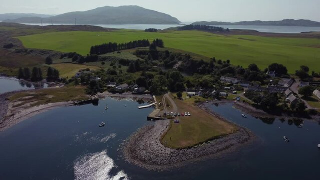 A high orbital done shot of a tiny village and harbour on a remote Scottish island eventually revealing the wider island and distant sea. Shot on the remote Scottish island of Luing in Summer