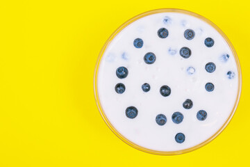 Glass bowl of yogurt with fresh blueberries on yellow background.