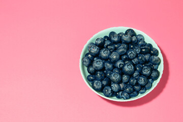 Fresh blueberry in bowl on pink background. Space for text. Concept of healthy and dieting eating