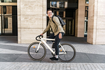 A young programmer guy riding to work on a bicycle with a bag, to the office on an eco-transport, a...
